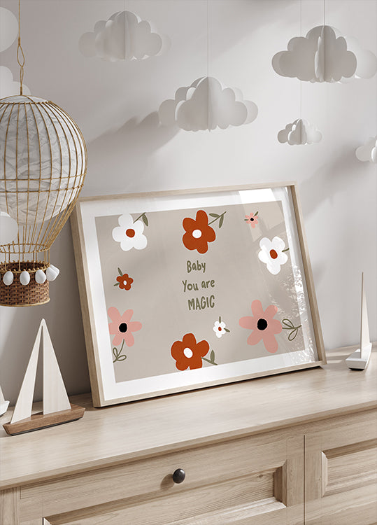 Oprawiona grafika z kwiatowym wzorem i napisem „Baby You are Magic” umieszczona jest na drewnianej komodzie, nad którą wisi dekoracyjna papierowa latarnia.